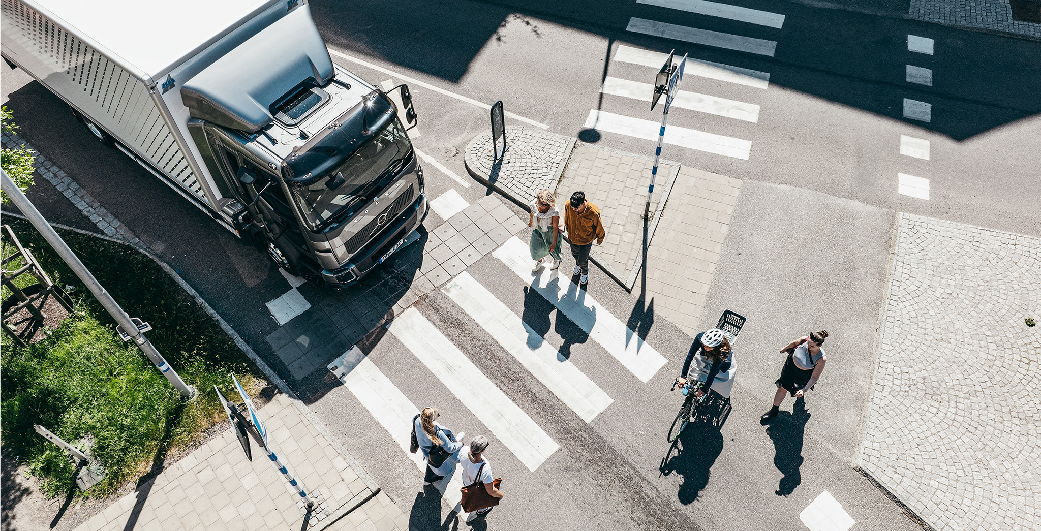 Overhead view of a Volvo truck stopped at a pedestrian crosswalk with people crossing the street in an urban area.